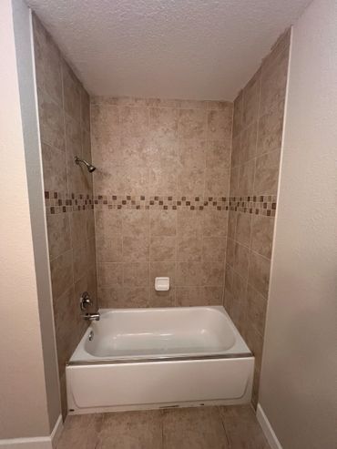 Clean bathtub with beige tiled walls and decorative border.
