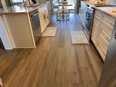 Modern kitchen with wooden floors, white cabinets, and a dining table by a large window.