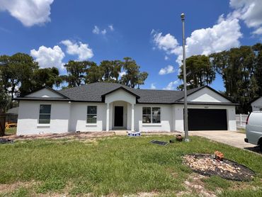 Modern single-story white house with black roof and garage under a sunny blue sky.
