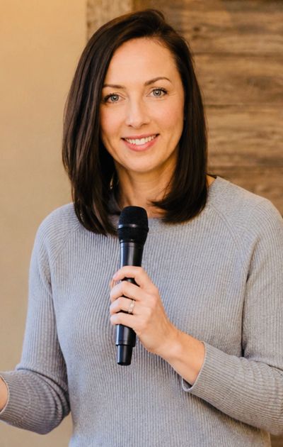 Woman in gray sweater holding a microphone and smiling.