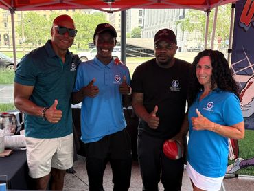 Four smiling people under a red tent giving thumbs up.