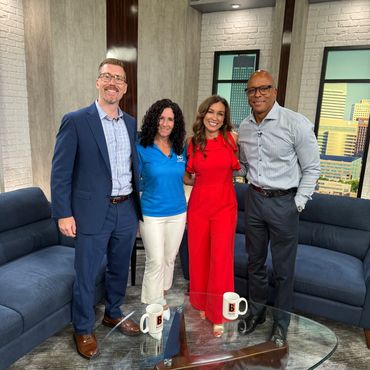 Four smiling people standing in a TV studio with coffee mugs on a glass table.