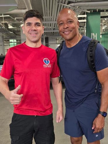 Two men standing in a parking garage, smiling at the camera.