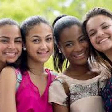 Four young women smiling closely together outdoors.