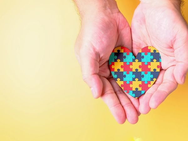 Hands holding a heart-shaped puzzle piece with colorful jigsaw pattern.