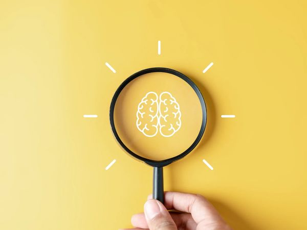 Magnifying glass highlighting a brain icon on a yellow background.