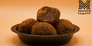 Traditional brown jaggery balls in a black bowl with a warm orange background.