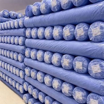 Stacks of blue fabric rolls wrapped in plastic and labeled.