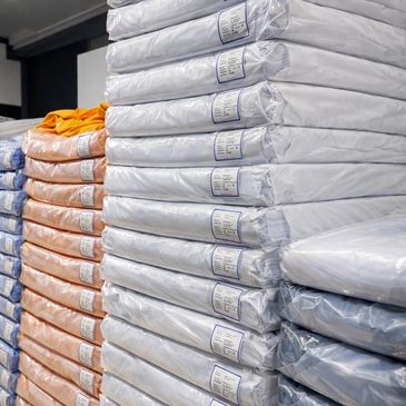 Stacks of packaged textiles or fabric rolls in white, orange, and blue colors.