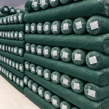 Stacks of green fabric rolls neatly arranged on shelves in a warehouse.