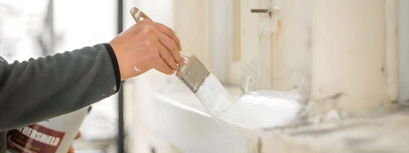 A man painting a windowsill white.