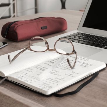 Glasses on a notebook with a laptop on a table for meeting notes 