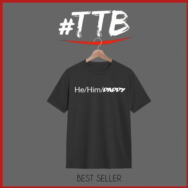 Black T-shirt with text 'He/Him/DADDY' hanging on a wooden hanger.