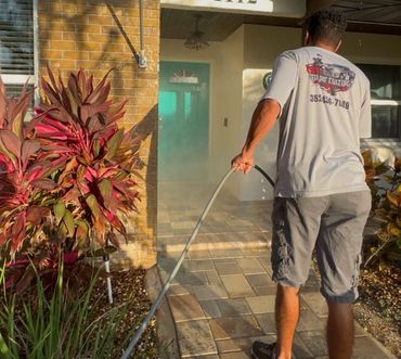 Man pressure washing a tiled porch outside a house.