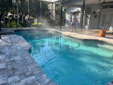 Two young men cleaning a backyard pool with hoses on a sunny day.