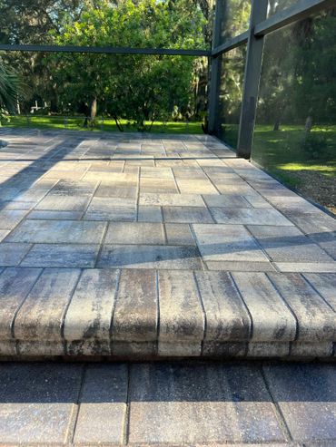 Sunlit patio with patterned stone tiles and glass enclosure.