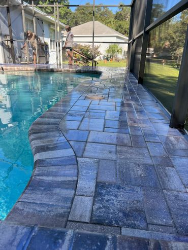 Two people cleaning a screened pool area with a hose and broom.