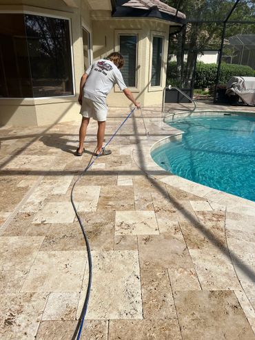 Person pressure washing poolside patio tiles on a sunny day.