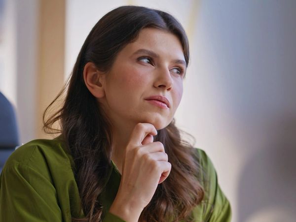 Young woman in green shirt thoughtfully looking away indoors.