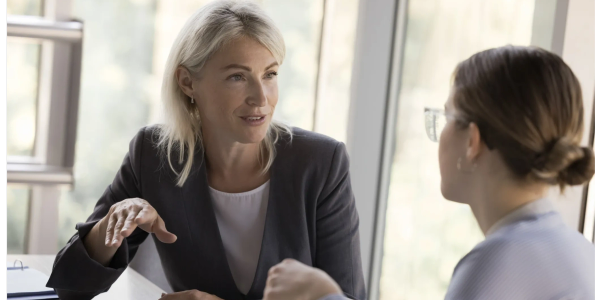 Two businesswomen engaged in a professional conversation at a desk.