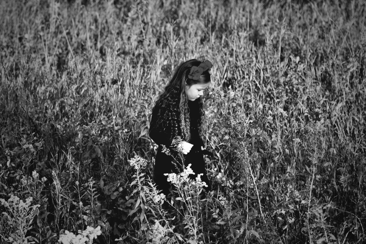 A young girl with a flower in her hair stands in a field of tall plants.