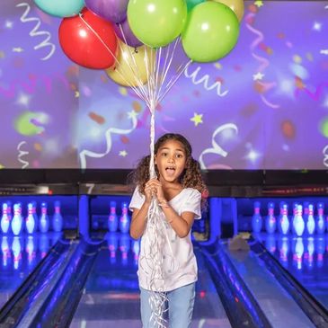 A joyful girl holding colorful balloons at a bowling alley.