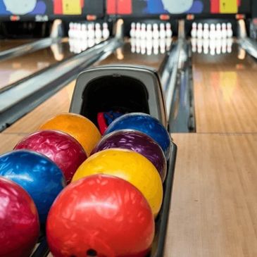 Colorful bowling balls lined up at a bowling alley with pins in the background.