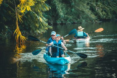 Two people kayaking on a calm river surrounded by greenery.