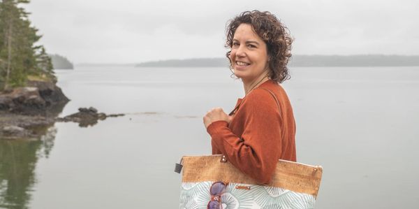 Photo of woman carrying oversize tote with ocean in background.