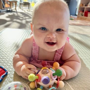 Smiling baby playing with a colorful toy on a textured mat.