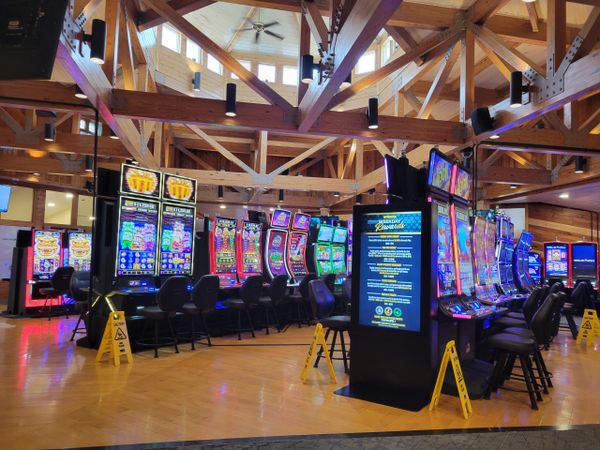 Slot machines in a spacious casino with wooden beams and ceiling fan.