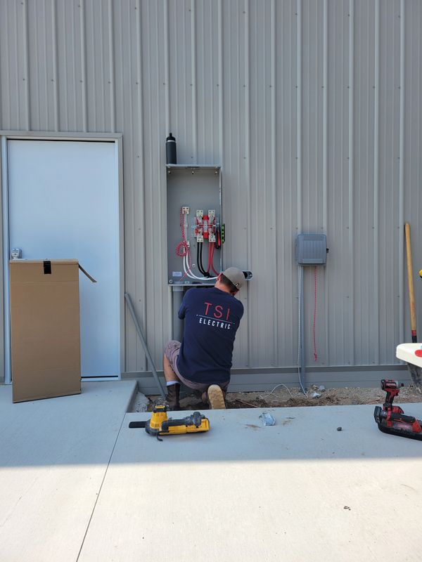 Electrician working on an electrical panel outside a metal building.