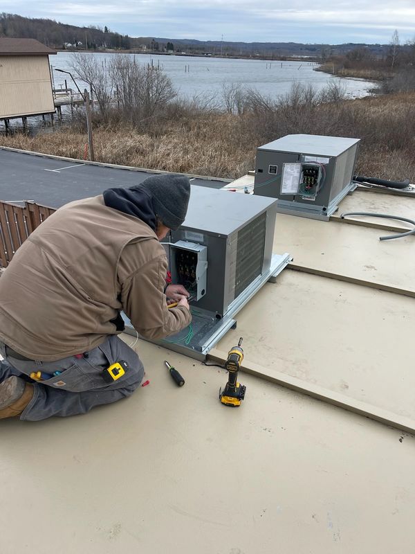 Technician repairing rooftop HVAC units on a cloudy day near a lake.