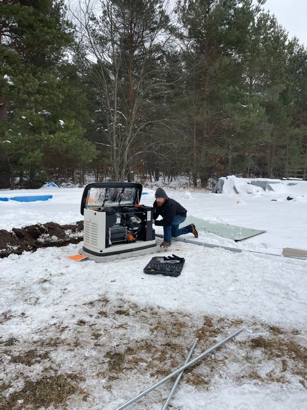 Man working on a generator outdoors in snowy forest.