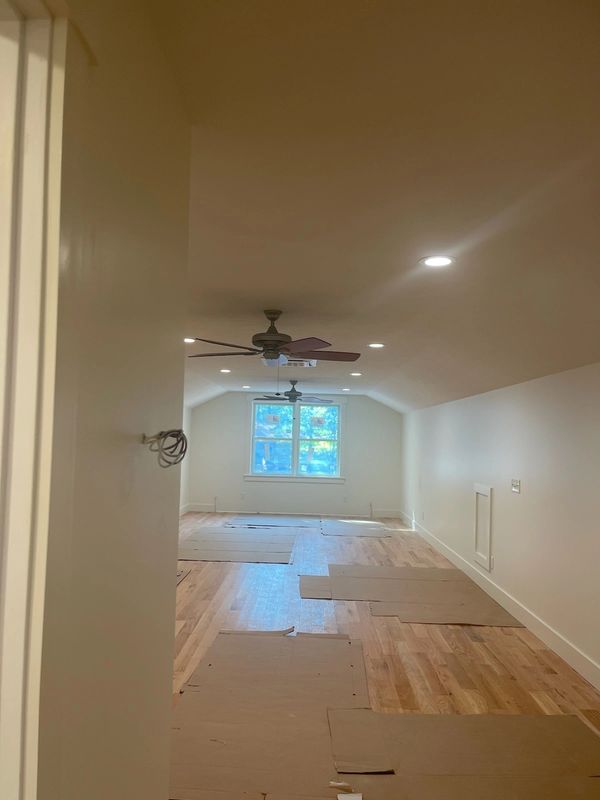Empty attic room with wooden floor and ceiling fans under recessed lights.