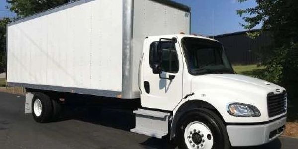 A large white box truck parked on a street with trees in the background.