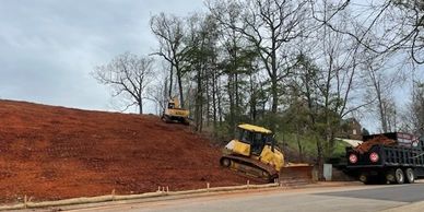 Construction vehicles working on a steep dirt hill beside a road.