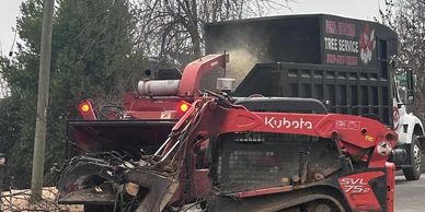 Kubota SVL75 skid steer loader working next to a tree service truck.