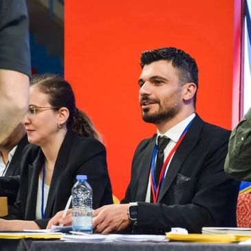 Resmi kıyafetli iki kişi toplantıda oturuyor.
