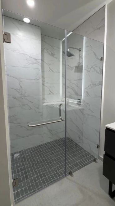 Modern shower with glass doors and marble-style tiles.