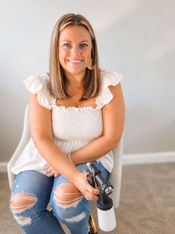 Smiling woman holding a spray gun sitting on a chair.