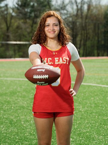 Young female athlete in red uniform holding a football on a field.