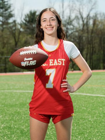 Young female athlete in red uniform holding a football on a field.