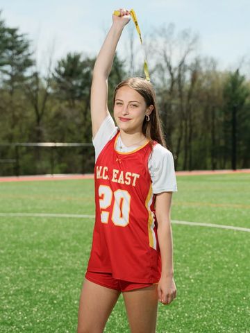 Young female athlete in red uniform holding a medal above her head on a sports field.