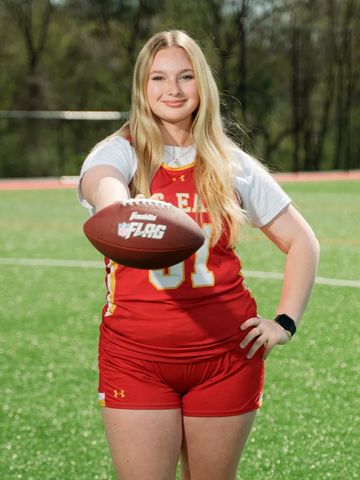 Young female athlete in red sports uniform holding a football on a field.