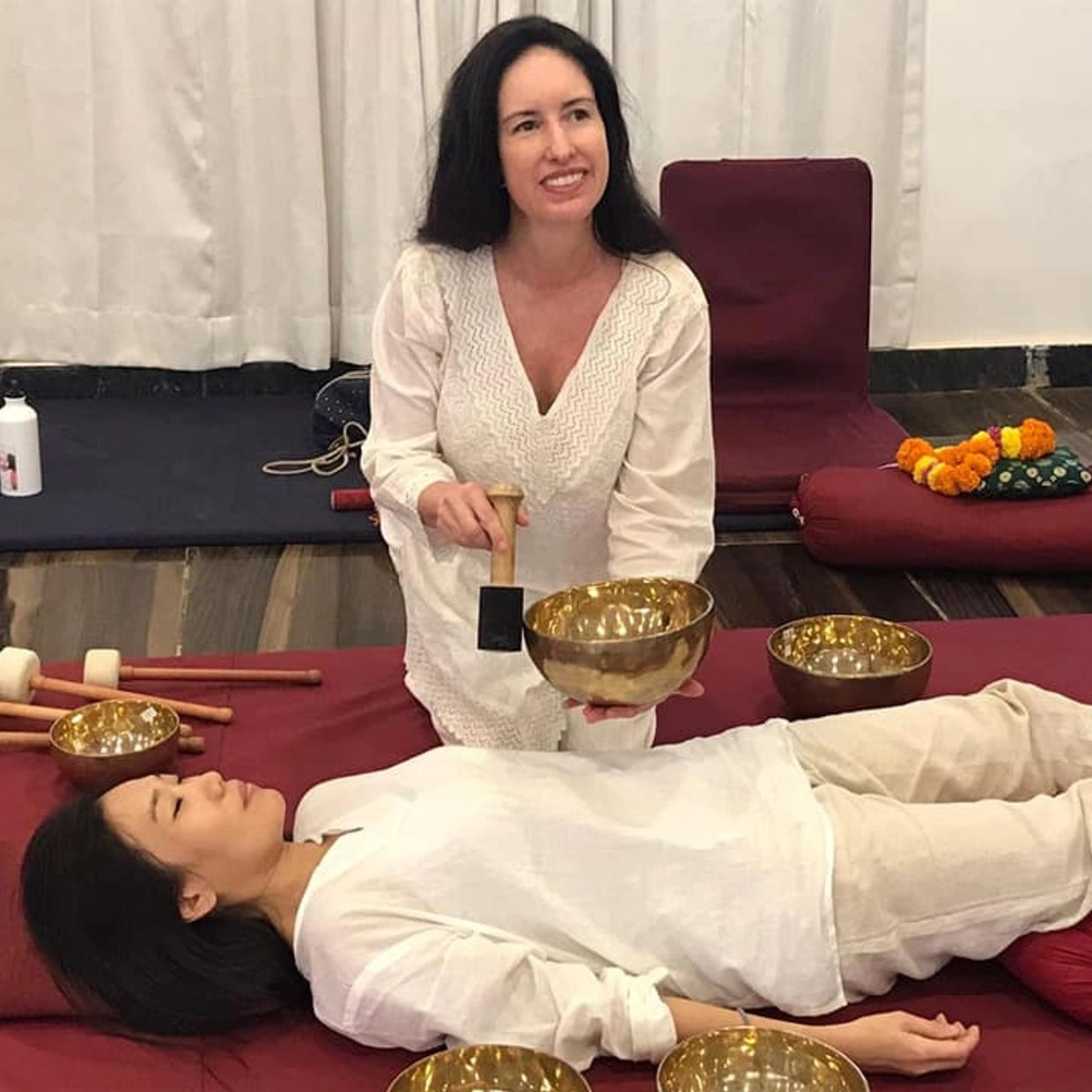 A woman performs sound therapy on a lying patient using Tibetan singing bowls.