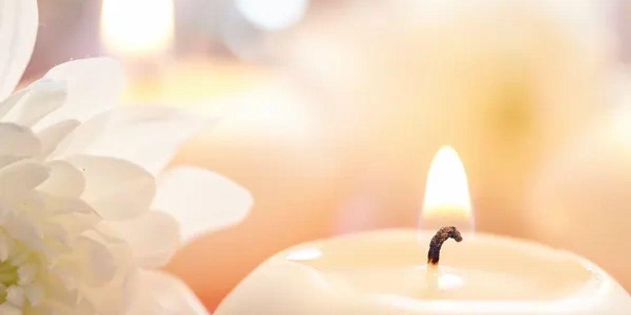 Close-up of a lit candle with white flowers in soft focus.