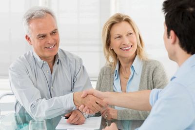 Two men shaking hands with a smiling woman observing.
