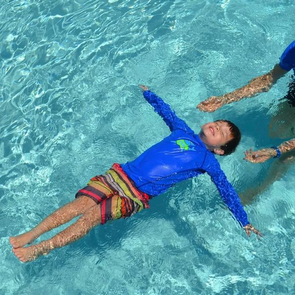 A child joyfully floats on water in a pool, supported by an adult.