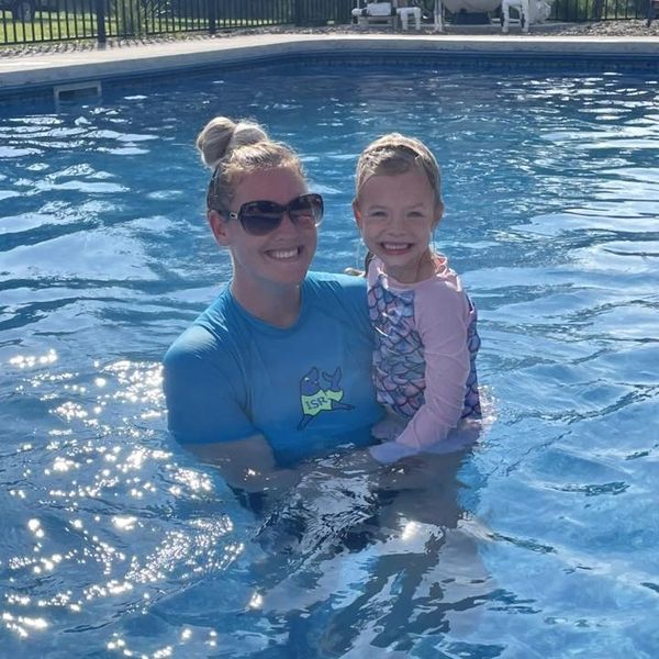 A woman and a girl smiling in a swimming pool on a sunny day.
